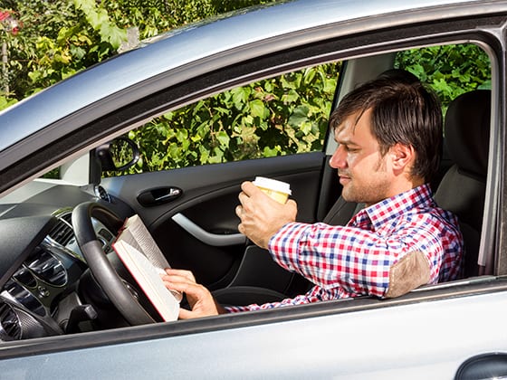Man reading a book and drinking coffee while driving