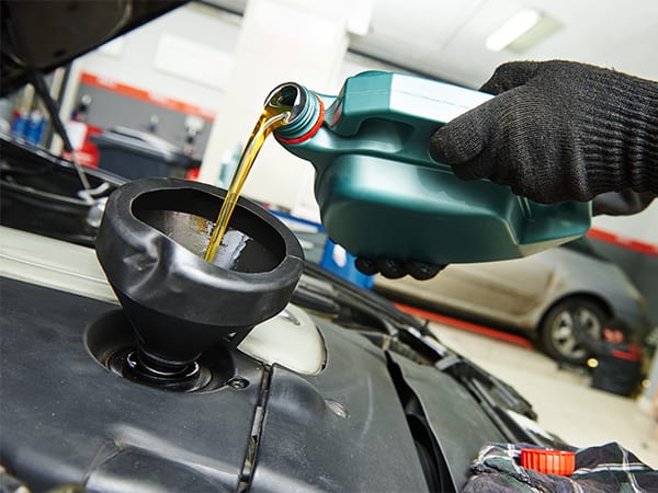 Mechanic adding pouring oil through a funnel into a car engine